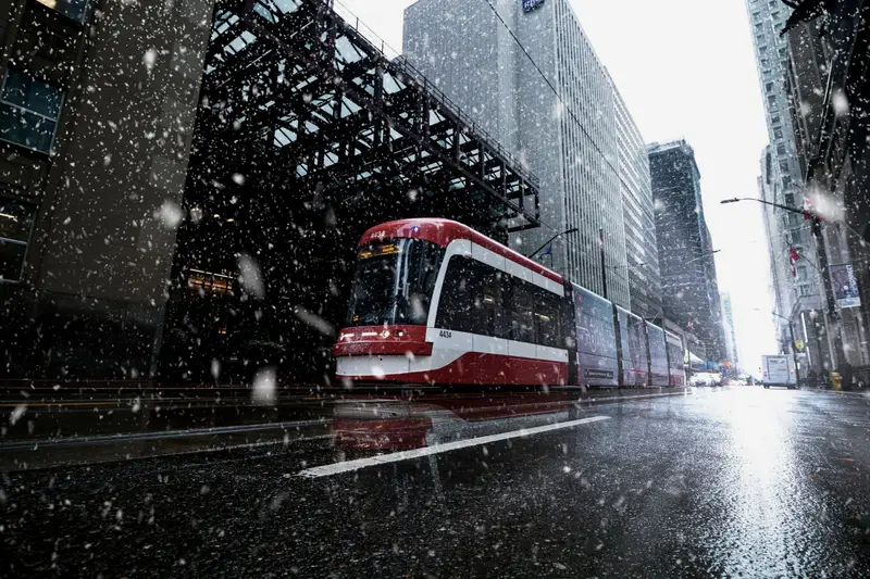 A red-and-white Toronto streetcar travelling through falling snow between downtown towers