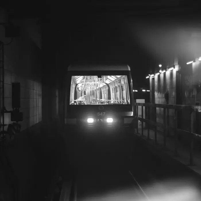 A subway train with its headlights on arriving along a dark station platform