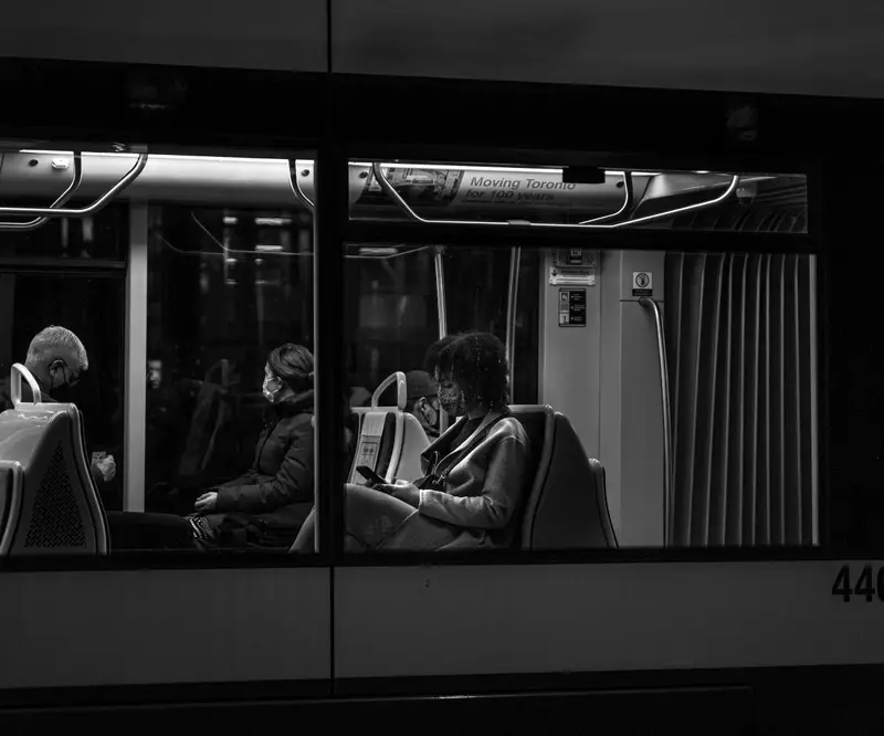Passengers seated on a city bus at night, seen through the windows